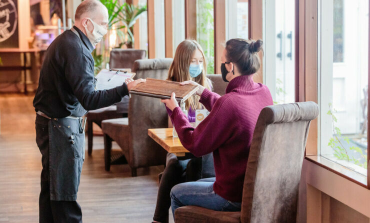 Wirtschaft in Corona-Zeiten (im Bild: Kellner reicht dem Gast eine Speisekarte)